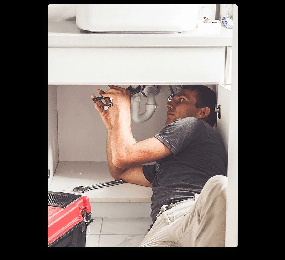 A plumber lies on his back under a sink