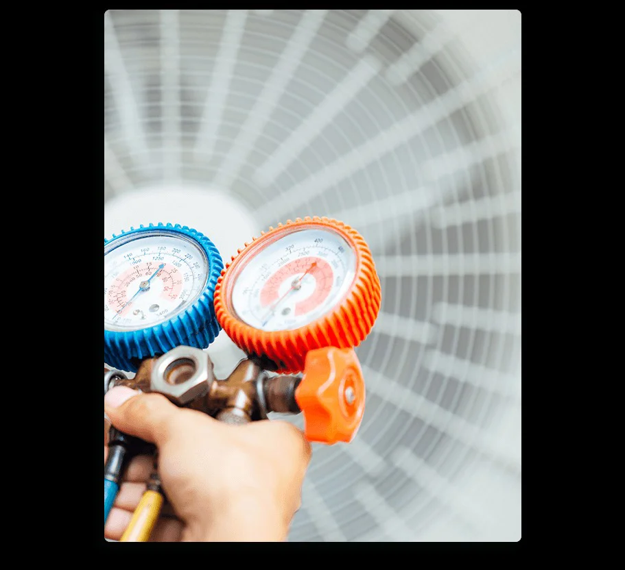 A technician's hand holds red and blue pressure gauges during AC maintenance