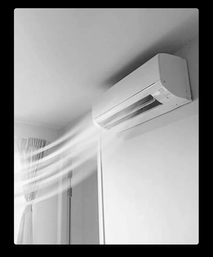 A ductless mini-split air conditioning unit is mounted high on a wall, actively blowing cool air
